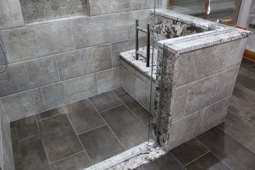 Grey tiled shower with a seating and glass door.