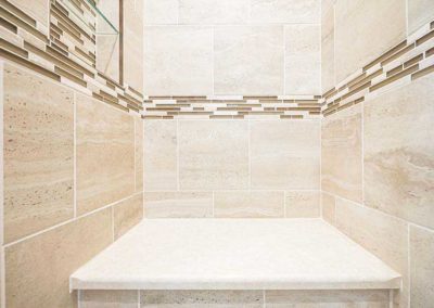Shower with beige wide tiles and a seating handicap accessible place.
