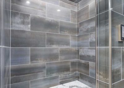 Wide dark tiled shower with a wheelchair accessible design and shower seating along the wall.