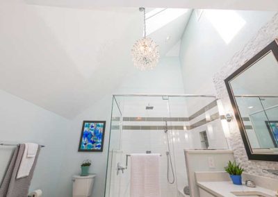 Bathroom with a glass shower and a triangular ceiling with natural light.