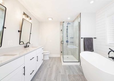 Master bathroom with white cabinets, wide tiles, a white bathtub and a glass shower.