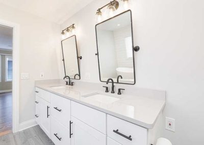 Master bathroom with white cabinets and countertops, double mirrors.