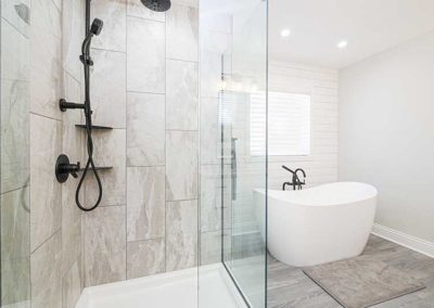 Bathroom with wide tiles, a white bathtub and a glass shower.