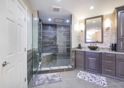 Bathroom with big wide floor tiles, big glass shower, and sink with dark wood cabinets.
