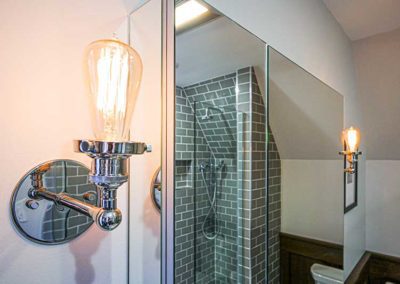 Bathroom with a mirror pointing to a glass shower with brick walls.