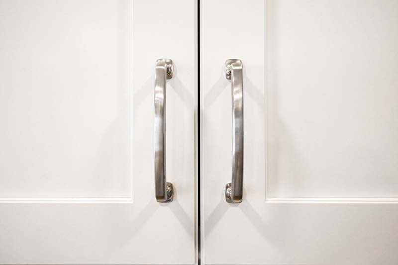 Close up of white cabinet doors with metal handles.