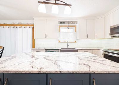White granite countertops in a kitchen with white cabinets and grey island.