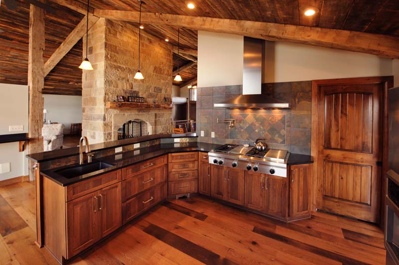 Rustic open space kitchen with dark wood cabinets, black countertops and a stone fireplace.