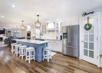 Big open space kitchen with white cabinets, granite countertops, grey-blue island and modern appliances.