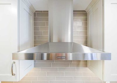 Kitchen metal chimney style hood next to white cabinets.