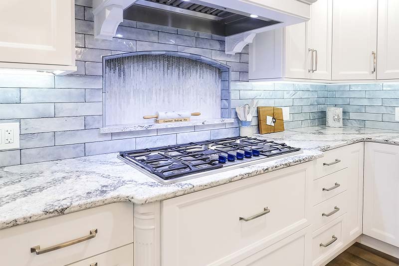 Kitchen with white cabinets, granite countertops, light blue backsplash, and a gas stovetop.