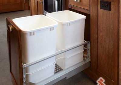 Unique storage space for trash cans inside wooden kitchen cabinets.